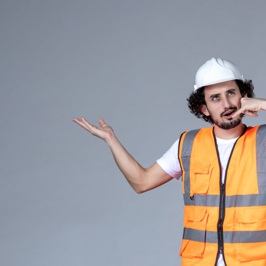 close-up-view-surprised-male-architect-warning-vest-with-safety-helmet-pointing-something-right-side-making-call-me-gesture-gray-wave-wall